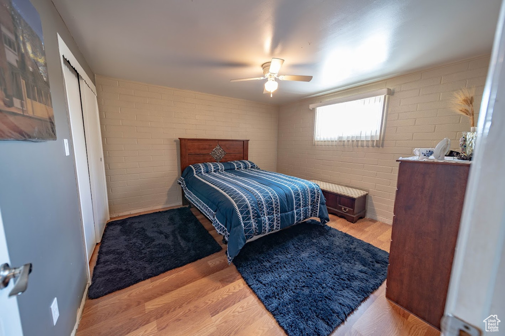 Bedroom featuring ceiling fan, a closet, brick wall, and wood-type flooring