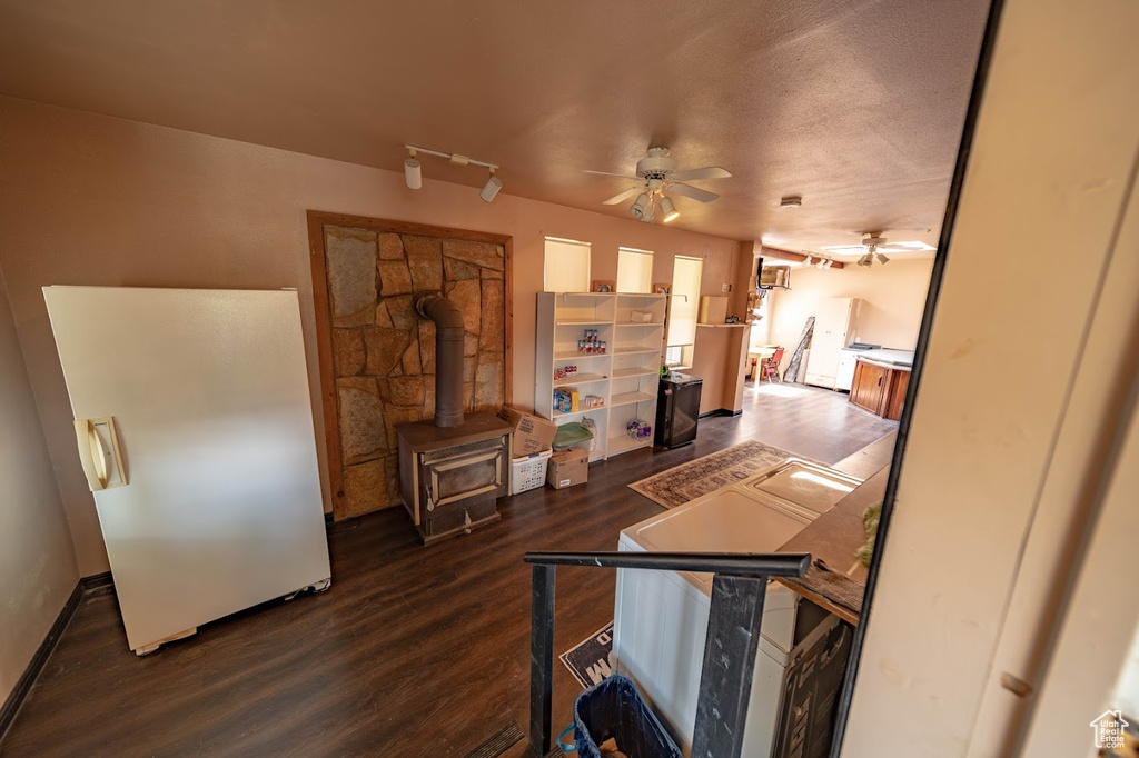 Living room with a textured ceiling, dark wood-type flooring, ceiling fan, and a wood stove