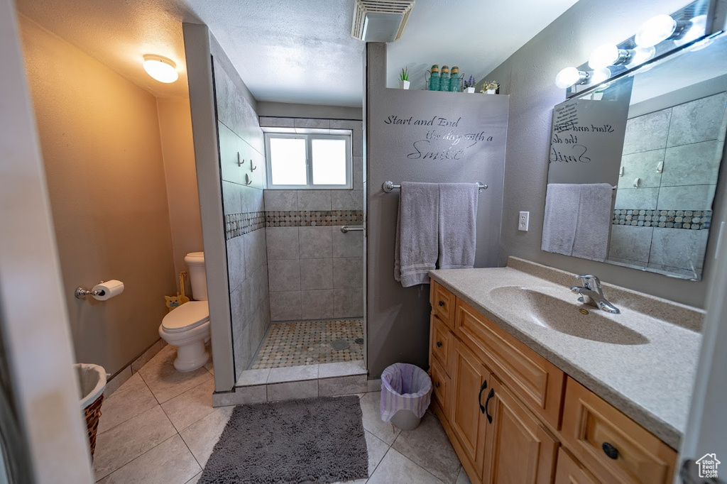 Bathroom featuring a tile shower, toilet, tile floors, and large vanity