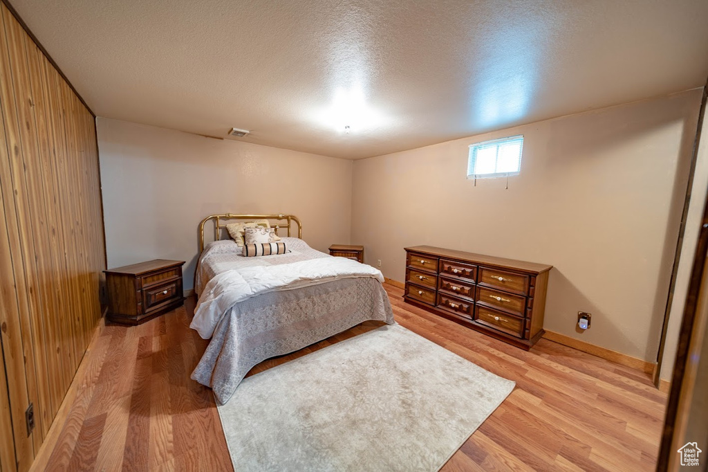 Bedroom featuring a textured ceiling, light hardwood / wood-style floors, and wood walls