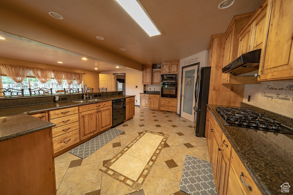 Kitchen featuring dark stone counters, sink, black appliances, and light tile floors