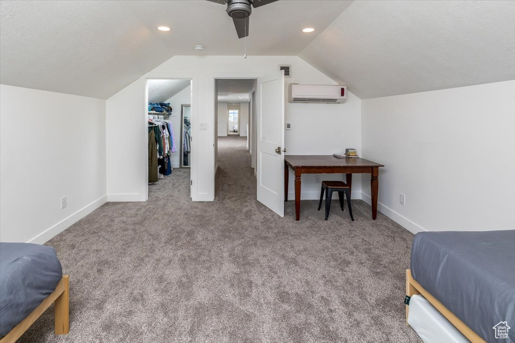 Bedroom featuring a wall unit AC, a walk in closet, carpet floors, and lofted ceiling