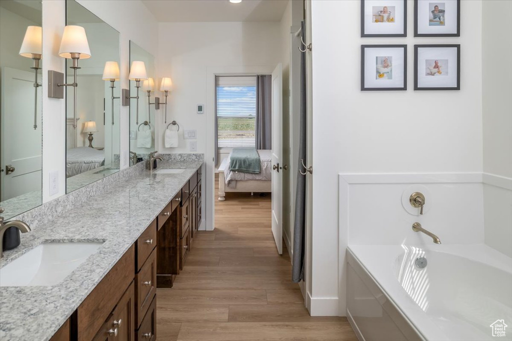 Bathroom with a bathtub, dual sinks, oversized vanity, and hardwood / wood-style floors