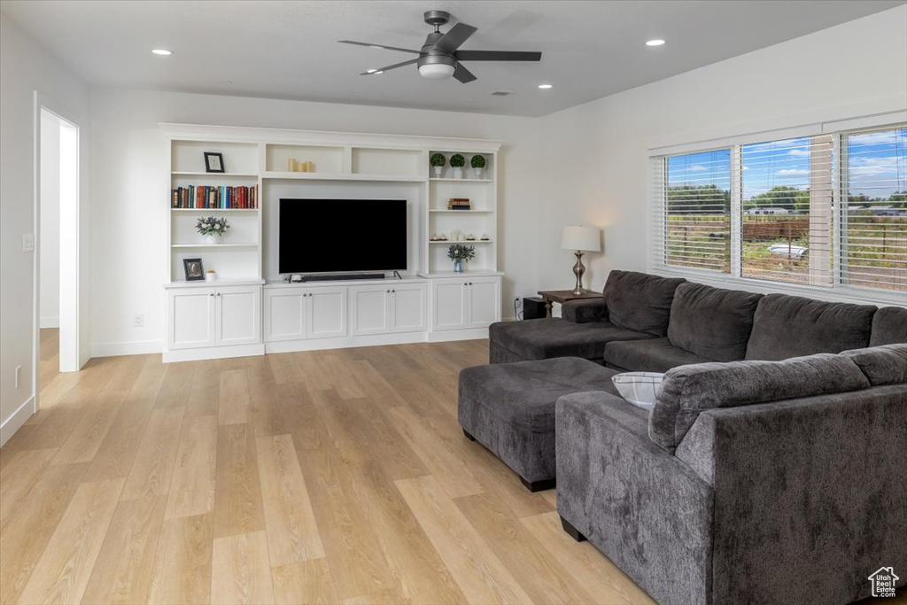 Living room with light hardwood / wood-style floors, built in shelves, and ceiling fan