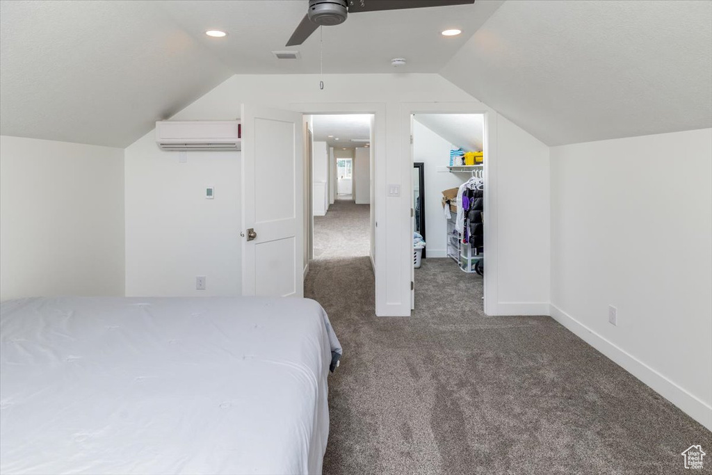 Carpeted bedroom featuring ceiling fan, a closet, an AC wall unit, lofted ceiling, and a walk in closet