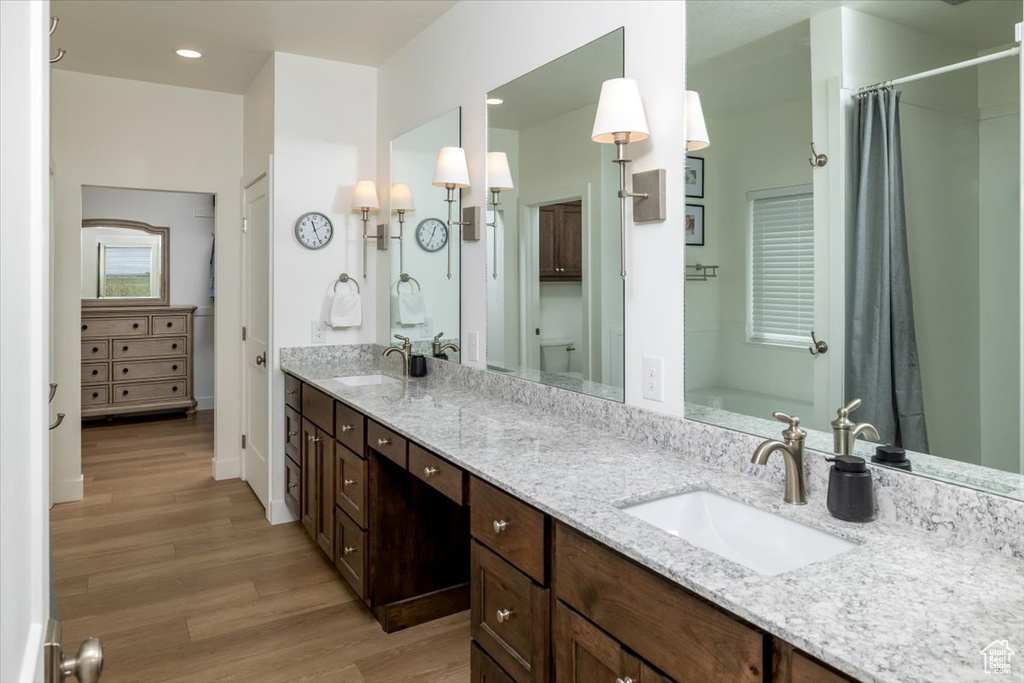 Bathroom featuring hardwood / wood-style flooring, oversized vanity, toilet, and double sink