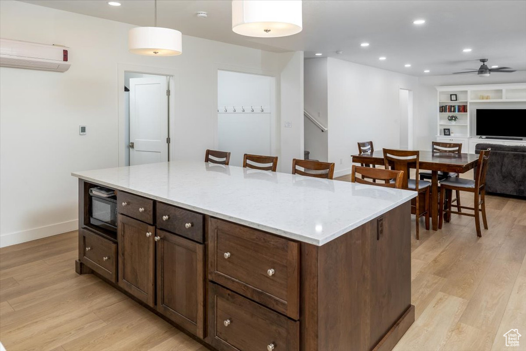 Kitchen featuring light stone countertops, light wood-type flooring, pendant lighting, black microwave, and a kitchen island