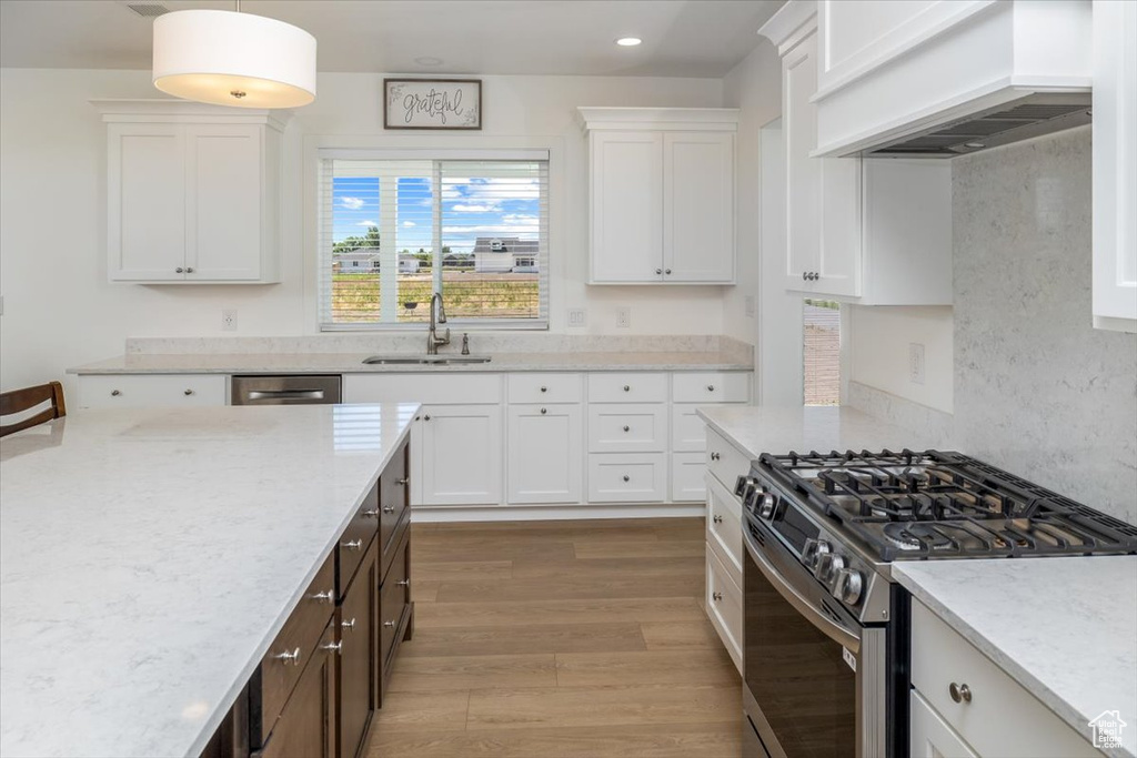 Kitchen featuring pendant lighting, wood-type flooring, custom range hood, sink, and appliances with stainless steel finishes