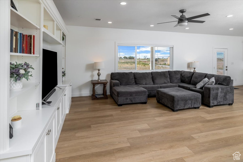 Living room with ceiling fan, built in shelves, and light wood-type flooring