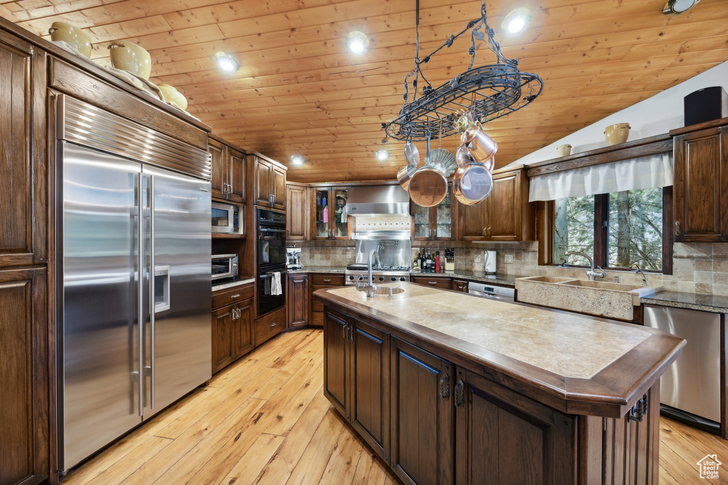 Kitchen featuring an island with sink, built in appliances, light hardwood / wood-style flooring, and backsplash