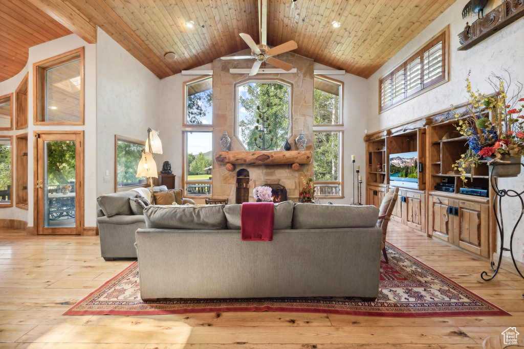 Living room with light hardwood / wood-style flooring, ceiling fan, a stone fireplace, wood ceiling, and high vaulted ceiling