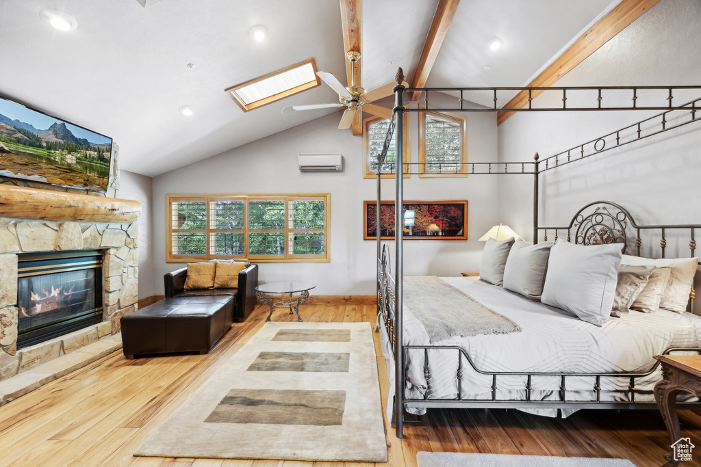 Bedroom featuring a stone fireplace, a wall mounted AC, beam ceiling, wood-type flooring, and a skylight