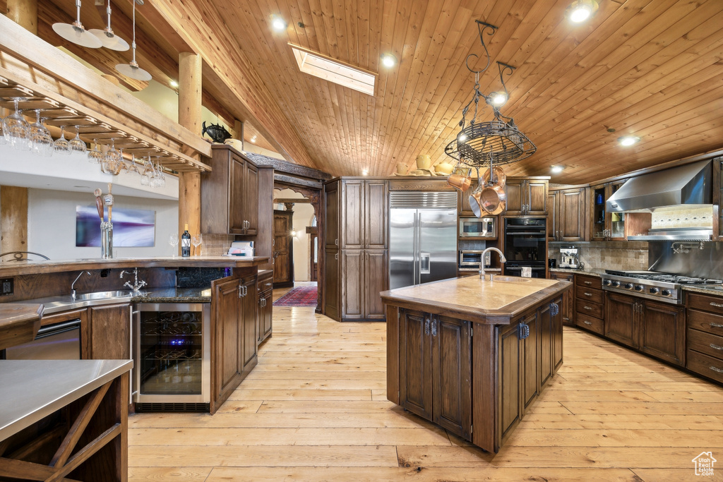 Kitchen featuring built in appliances, a kitchen island with sink, backsplash, and light hardwood / wood-style floors