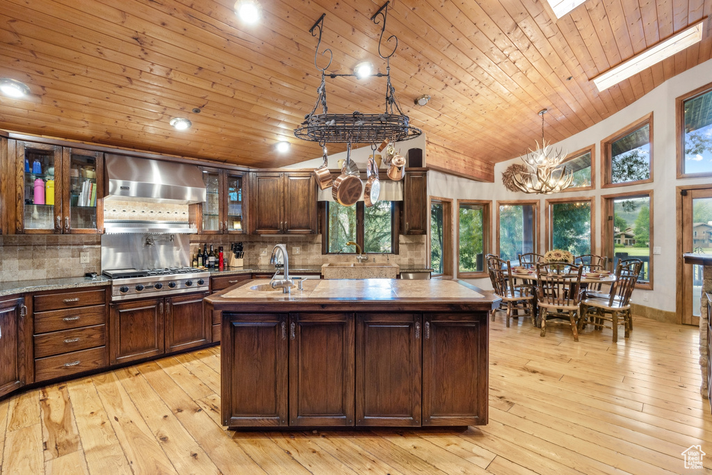 Kitchen featuring wall chimney exhaust hood, light hardwood / wood-style floors, a skylight, and backsplash