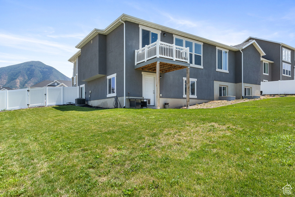 Back of property with a mountain view, a balcony, a lawn, and central AC unit