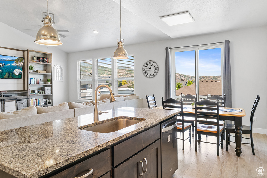 Kitchen featuring decorative light fixtures, light wood-type flooring, sink, dishwasher, and dark brown cabinetry