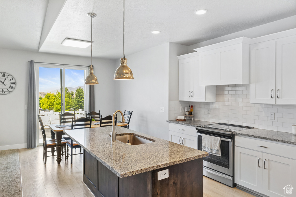 Kitchen featuring tasteful backsplash, white cabinets, light wood-type flooring, sink, and stove