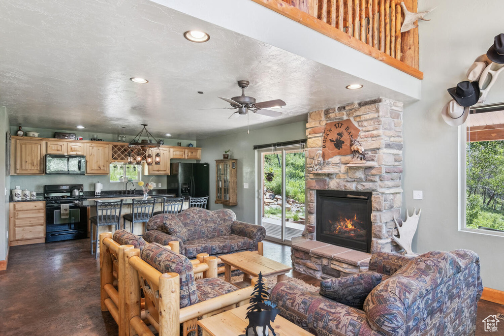 Living room featuring sink, a stone fireplace, ceiling fan, and a textured ceiling