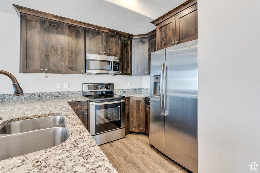 Kitchen featuring light stone counters, dark brown cabinetry, light hardwood / wood-style floors, appliances with stainless steel finishes, and sink