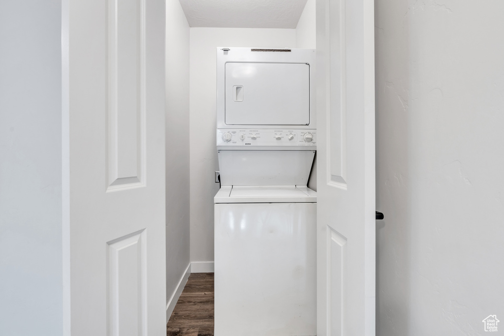 Clothes washing area featuring dark wood-type flooring and stacked washing maching and dryer