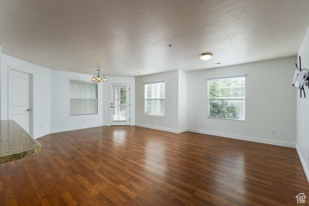 Unfurnished living room featuring a chandelier, a wealth of natural light, a textured ceiling, and dark hardwood / wood-style flooring