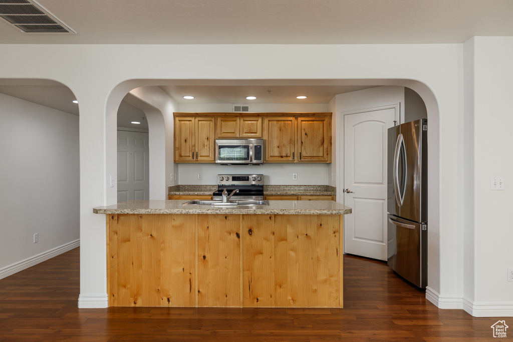 Kitchen with light stone counters, appliances with stainless steel finishes, sink, and dark hardwood / wood-style floors