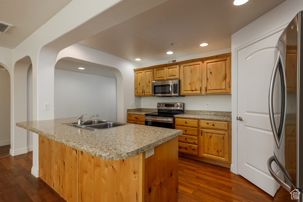 Kitchen with stainless steel appliances, sink, dark hardwood / wood-style flooring, and an island with sink