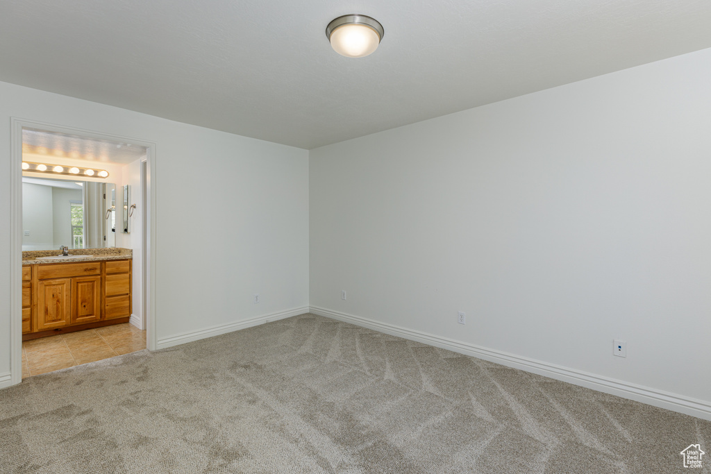 Unfurnished bedroom with light colored carpet, sink, and ensuite bath