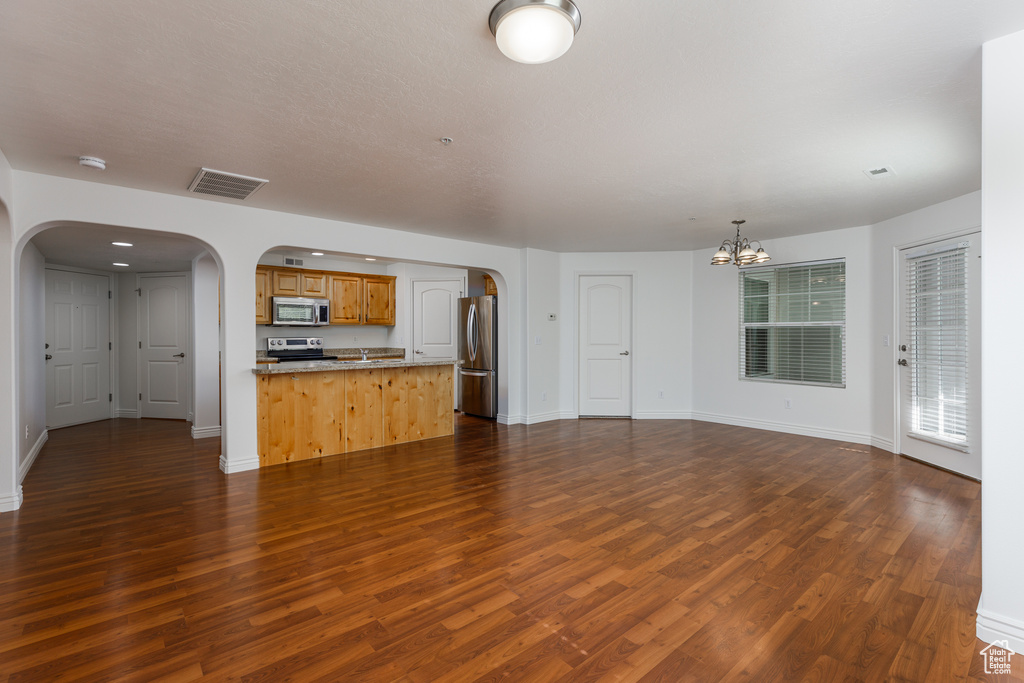 Unfurnished living room featuring dark wood-type flooring, sink, and an inviting chandelier