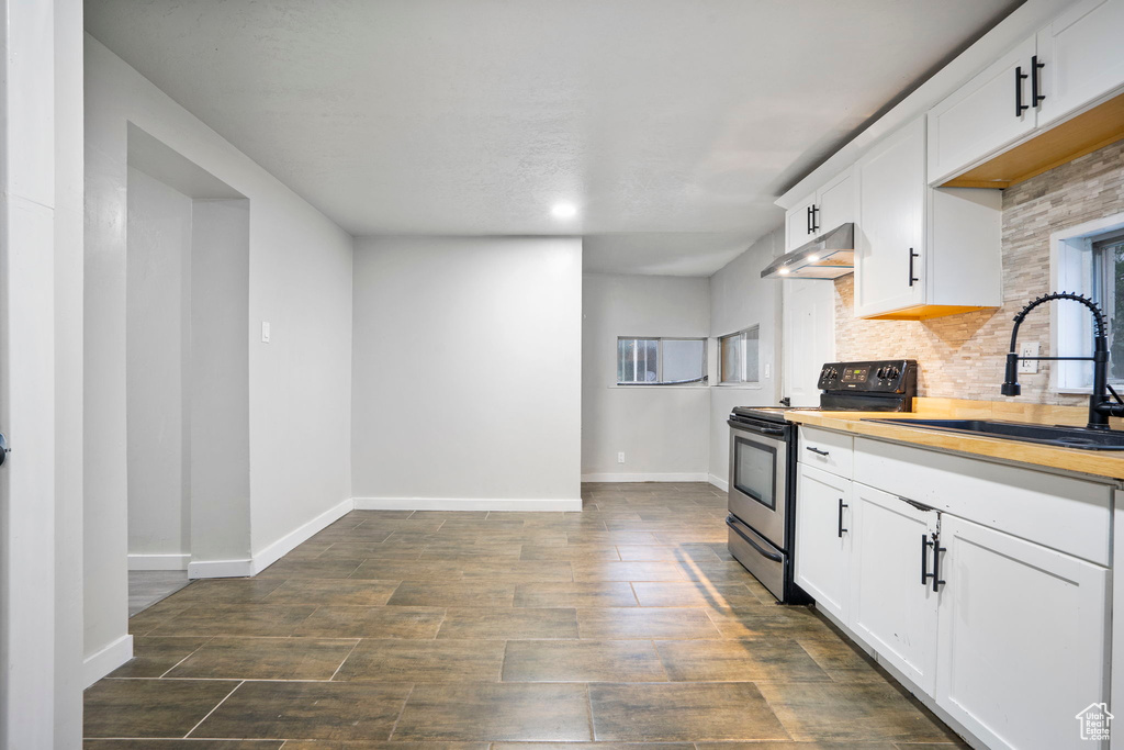 Kitchen with wood counters, white cabinets, electric stove, backsplash, and sink