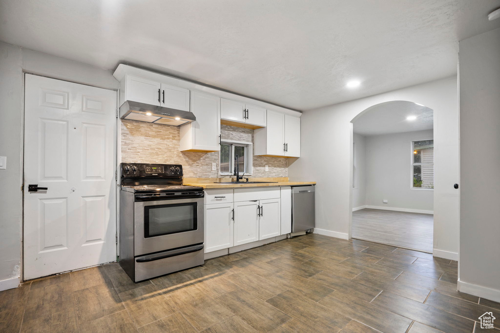 Kitchen featuring stainless steel appliances, white cabinets, wood-type flooring, sink, and tasteful backsplash