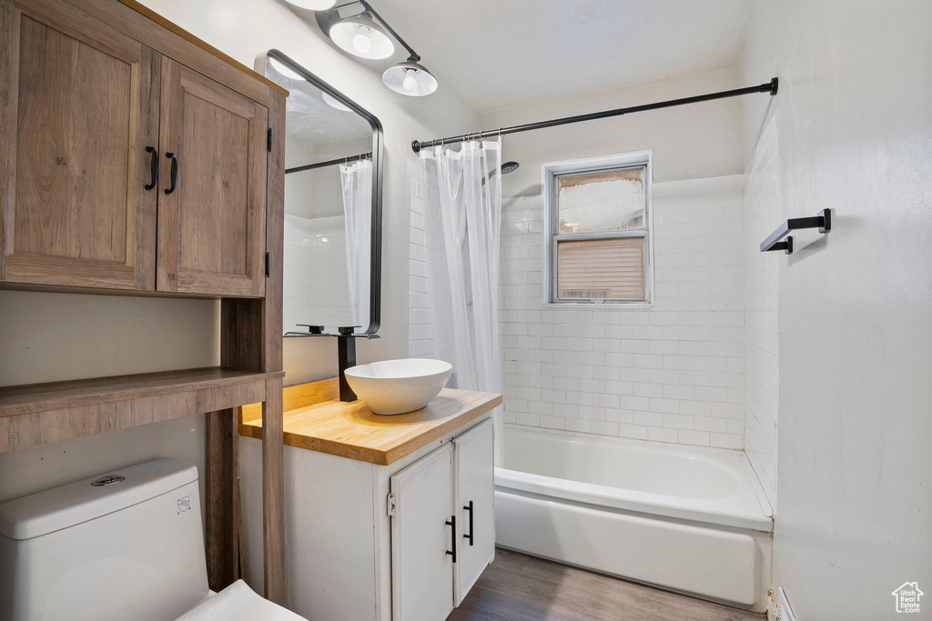 Full bathroom with oversized vanity, shower / tub combo with curtain, hardwood / wood-style flooring, and toilet