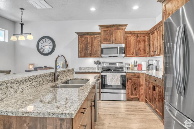 Kitchen with light stone counters, sink, decorative light fixtures, stainless steel appliances, and light hardwood / wood-style flooring