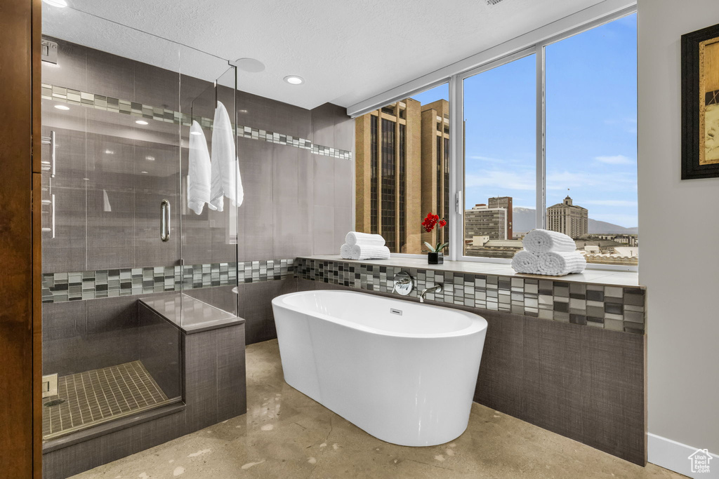 Bathroom with concrete floors, separate shower and tub, and tile walls