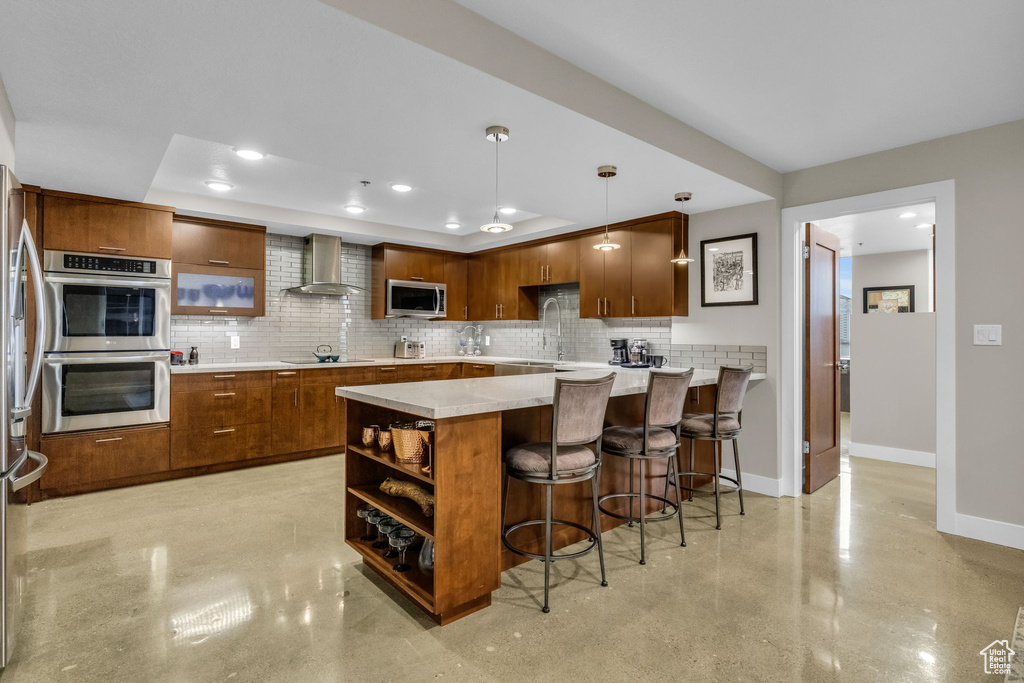 Kitchen with hanging light fixtures, backsplash, wall chimney exhaust hood, and stainless steel appliances