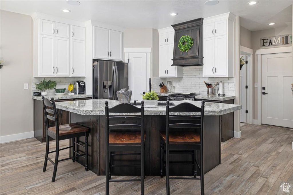 Kitchen featuring light stone countertops, light hardwood / wood-style flooring, stainless steel fridge, backsplash, and a breakfast bar area