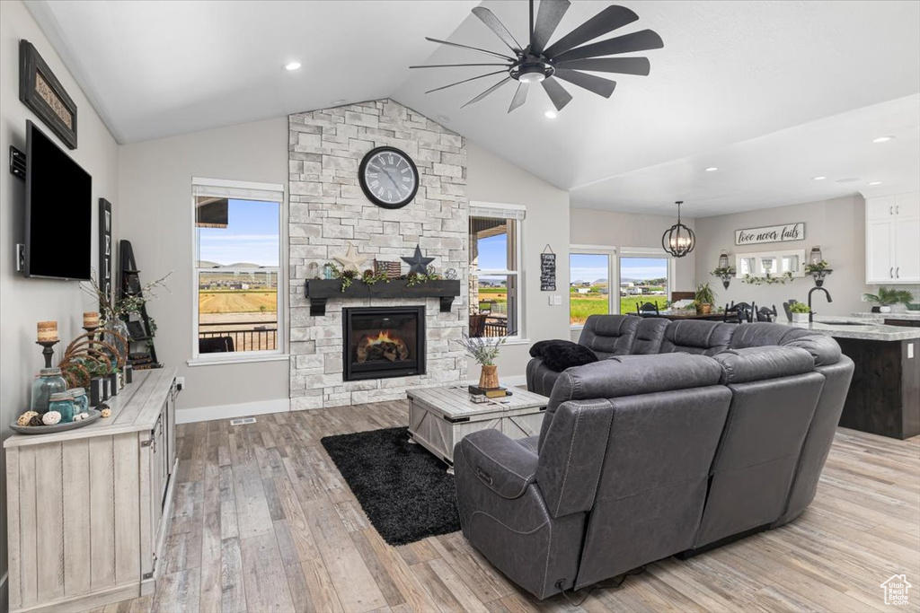 Living room featuring lofted ceiling, a fireplace, light wood-type flooring, and ceiling fan