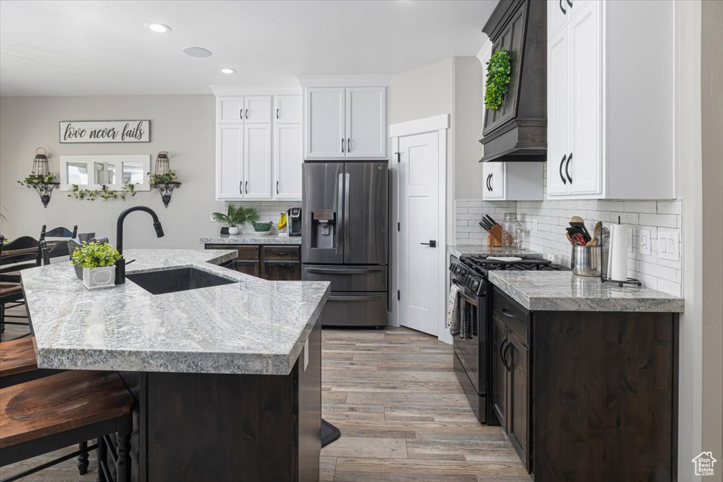 Kitchen with stainless steel fridge, an island with sink, wood-type flooring, gas range oven, and sink