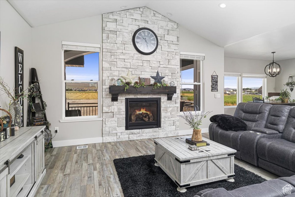 Living room featuring a notable chandelier, wood-type flooring, a stone fireplace, and vaulted ceiling