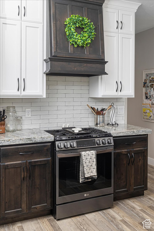 Kitchen with stainless steel gas range, white cabinets, backsplash, and light hardwood / wood-style flooring