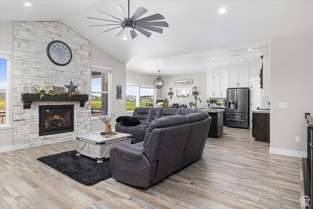 Living room featuring a stone fireplace, ceiling fan, light hardwood / wood-style floors, and lofted ceiling