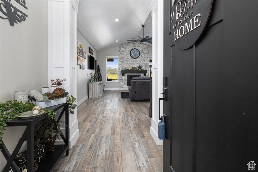 Foyer entrance with a stone fireplace, ceiling fan, vaulted ceiling, and hardwood / wood-style floors