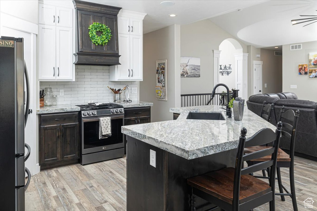 Kitchen with custom exhaust hood, stainless steel appliances, light wood-type flooring, sink, and white cabinets