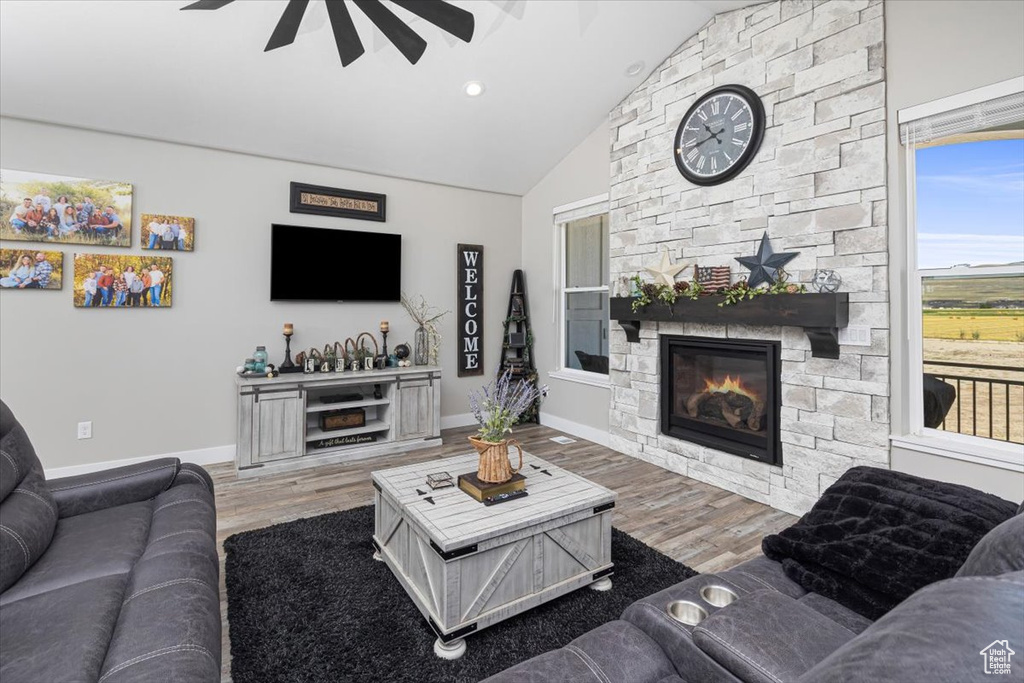 Living room featuring vaulted ceiling, a stone fireplace, hardwood / wood-style flooring, and ceiling fan