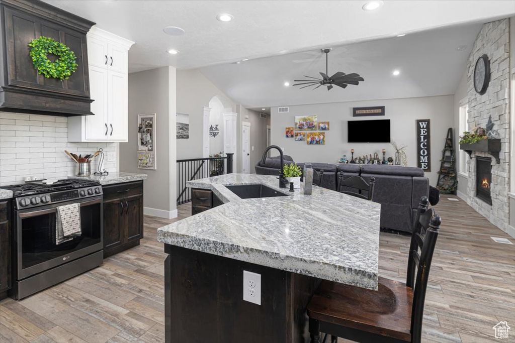 Kitchen with light hardwood / wood-style flooring, stainless steel range with gas stovetop, premium range hood, sink, and white cabinetry