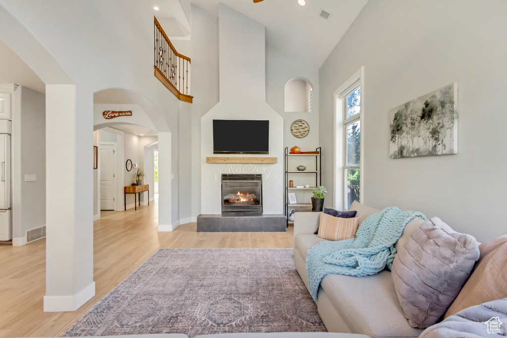 Living room with light hardwood / wood-style flooring, a tiled fireplace, high vaulted ceiling, and ceiling fan