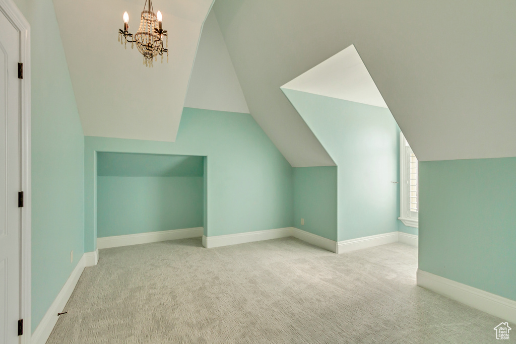 Additional living space with lofted ceiling, light carpet, and an inviting chandelier