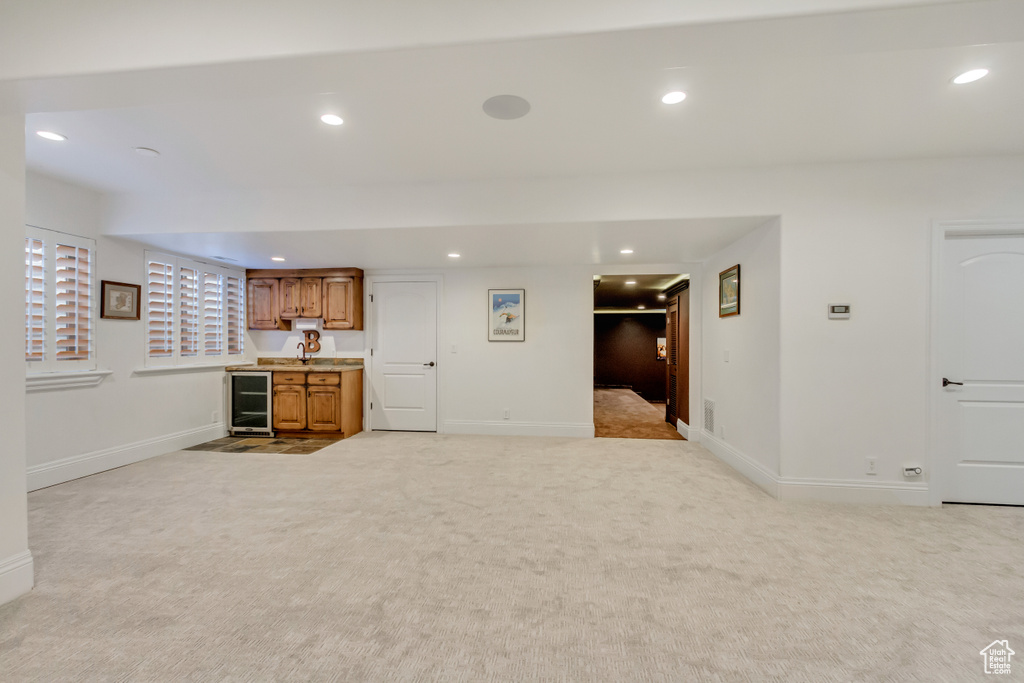 Unfurnished living room with wine cooler, light carpet, and bar area