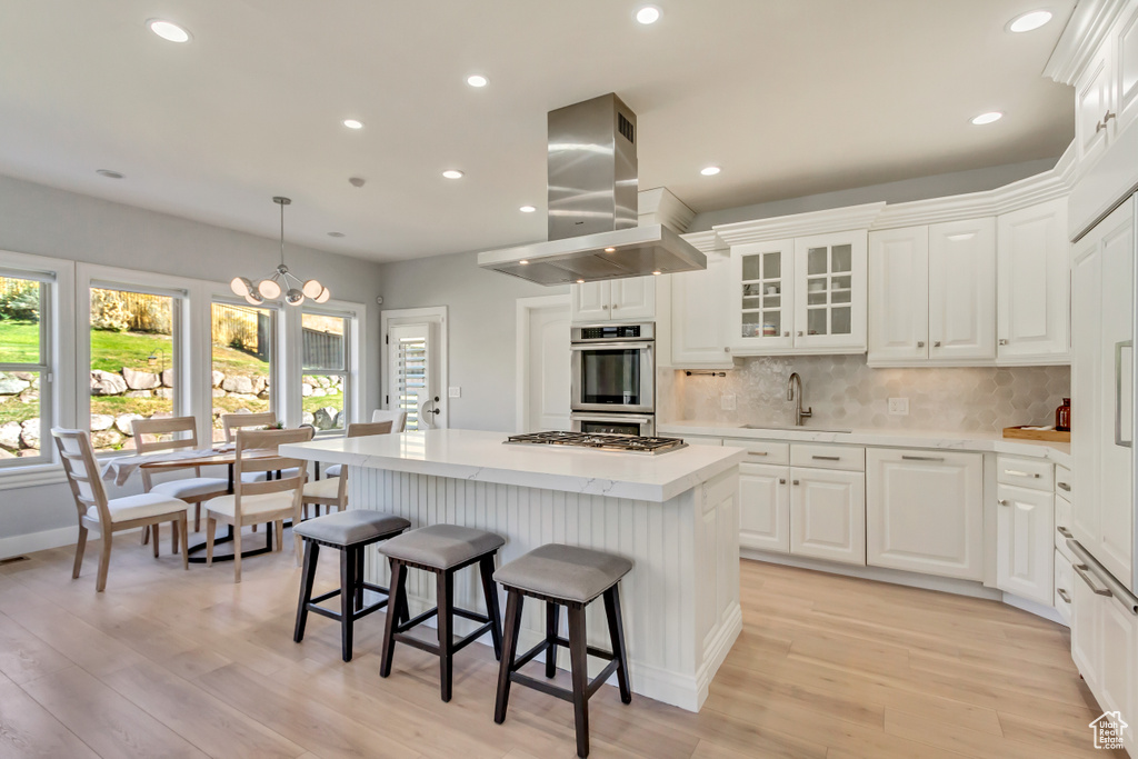 Kitchen featuring white cabinets, light hardwood / wood-style floors, a kitchen island, and island range hood