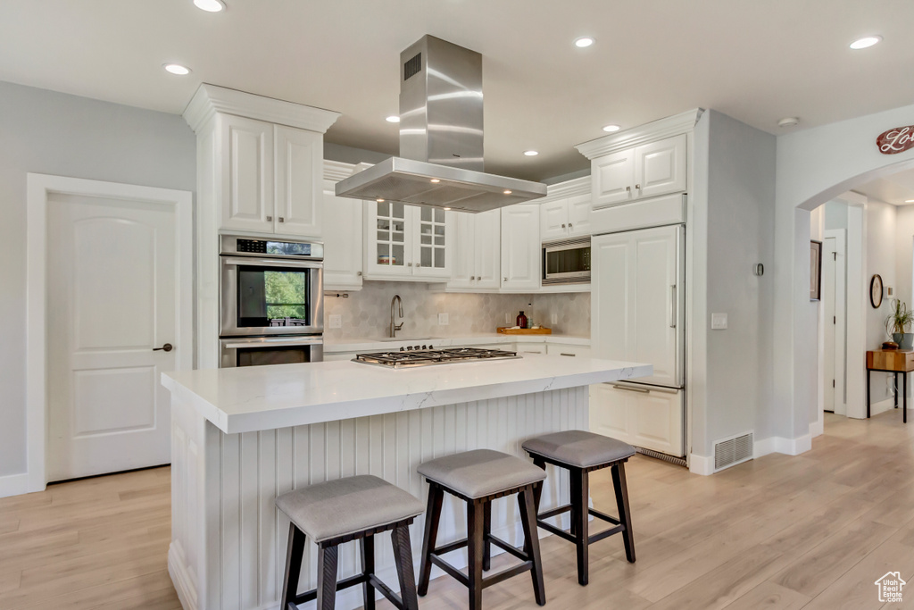 Kitchen with white cabinetry, built in appliances, island range hood, and light wood-type flooring